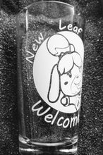 Load image into Gallery viewer, 16oz pint glass with image of Isabelle from Animal Crossing in a circle. She is smiling and her arms are open to give you a hug. Around the circle are the words "New Leaf Welcome Wagon".