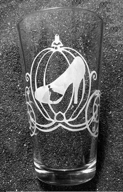 A pint glass with an etched Cinderella design. There is a silhouette of Cinderella running down the stairs, framed inside of a glass slipper. The slipper is superimposed on top of the classic pumpkin carriage. 