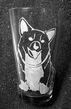 Load image into Gallery viewer, A pint glass with a corgi design. The Corgi faces the viewer, mouth open, tongue out, head tilted to the side. He is sitting and wearing a collar. 

