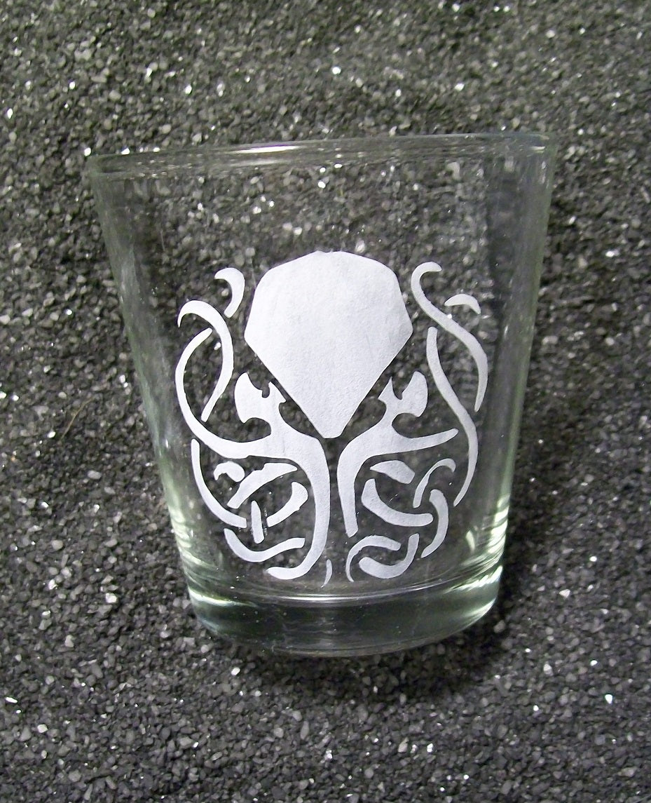A shot glass featuring an etched design of Cthulhu. His tentacles are twisted into a celtic knot formation. 
