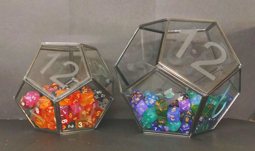 Two D12 terrariums sitting next to each other. The smaller D12 is half full of orange, pink, and black dice. The larger D12 is half-full of blue, green, and purple dice. Between the two terrariums there are 222 dice in the image. 