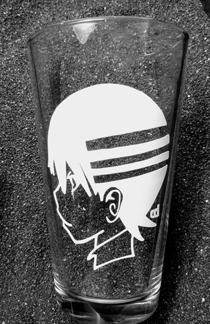 A pint glass with a design of Death the Kid from Soul Eater. A profile headshot, he is facing to the left so the viewer can see the three stripes in his hair. 