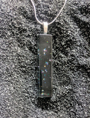 A long skinny rectangle pendant made of glass. The design is black glass with small clusters of glitter sprinkled throughout. 