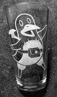 A pint glass etched with a prini design. The prini is dancing, its left flipper and left leg up in the air, it's mouth open in a grin. 